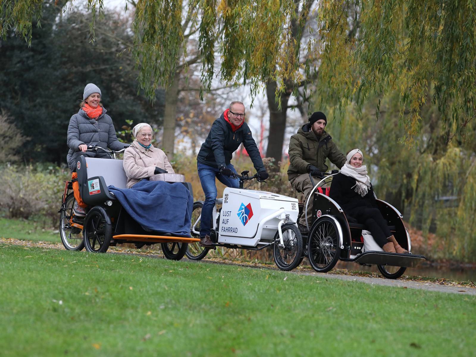 Eine Person fährt ein Lastenfahrrad, zwei weitere befördern Personen mit Fahrrad-Rikschas.